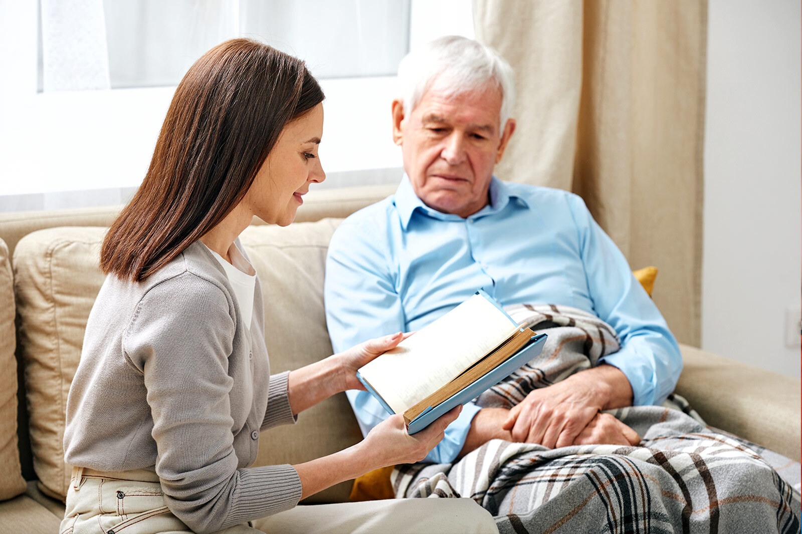 Care worker reads to elderly man sat on settee