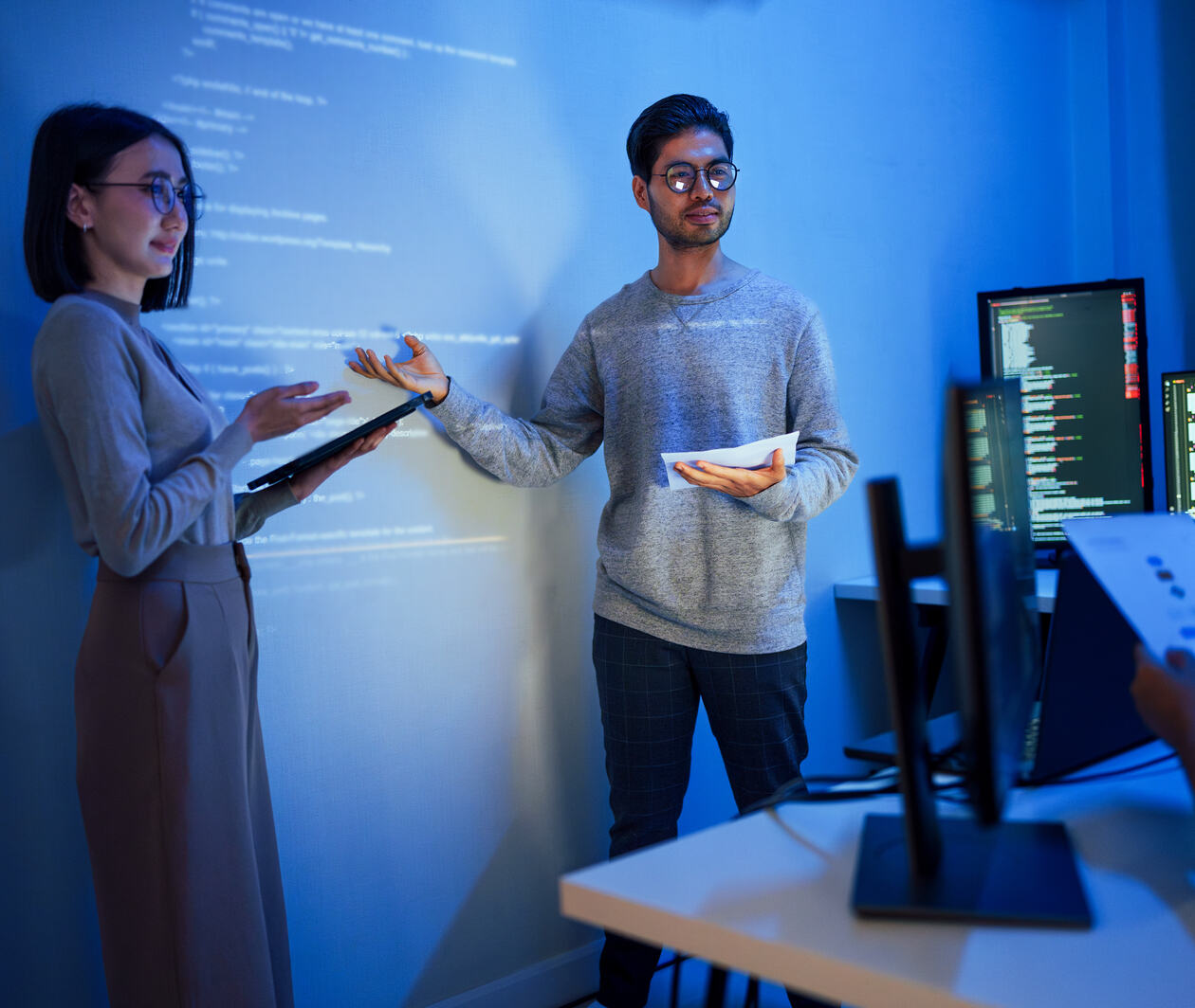 A man and a woman standing in front of a student who is taking notes on a monitor while they give a presentation