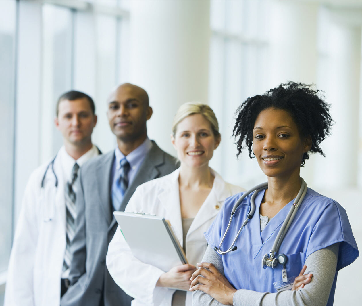 2 happy female wearing medics' uniforms standing before 2 male multi-ethnic medical professionals.