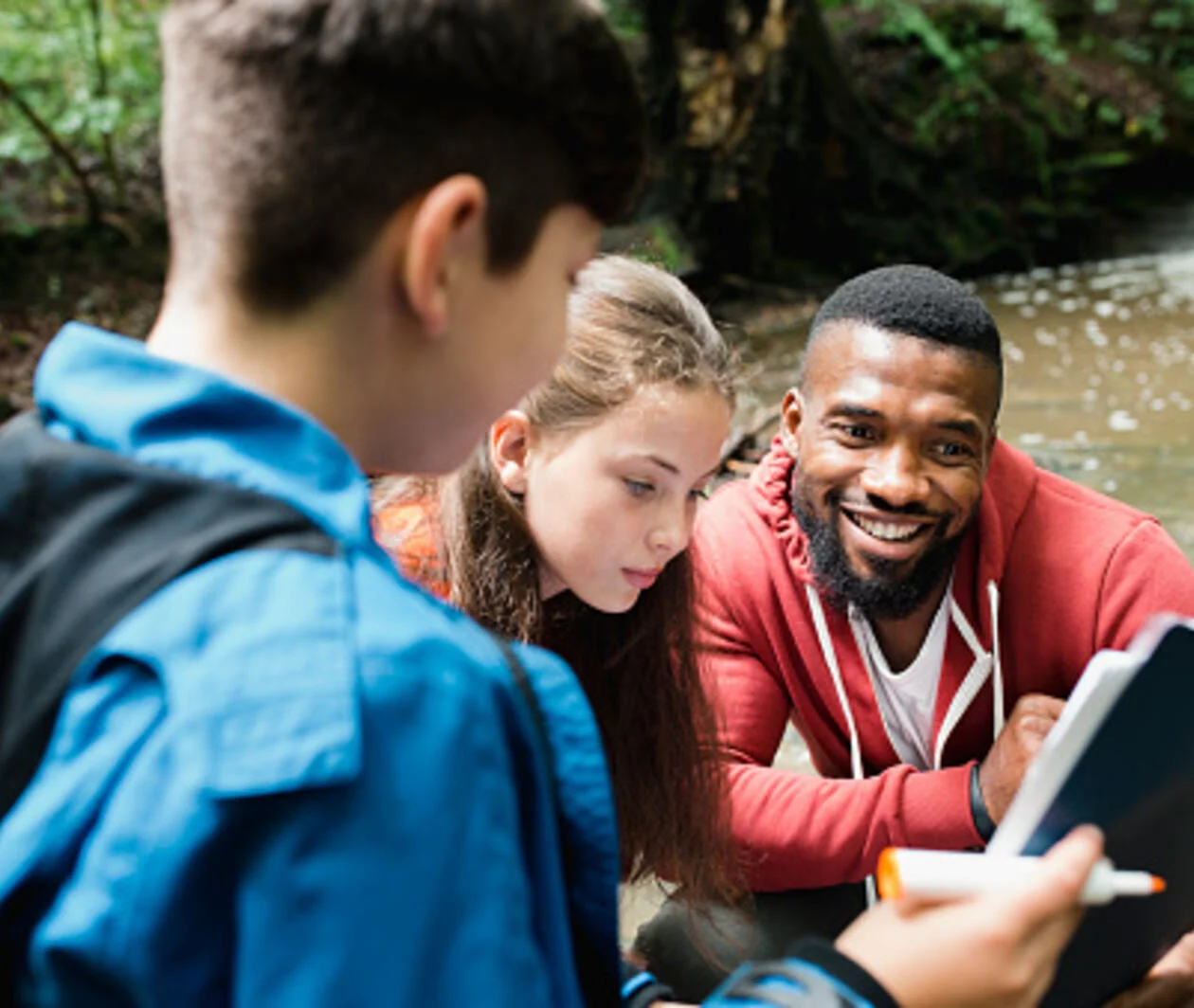 A group of people outside near a stream looking at a clipboard