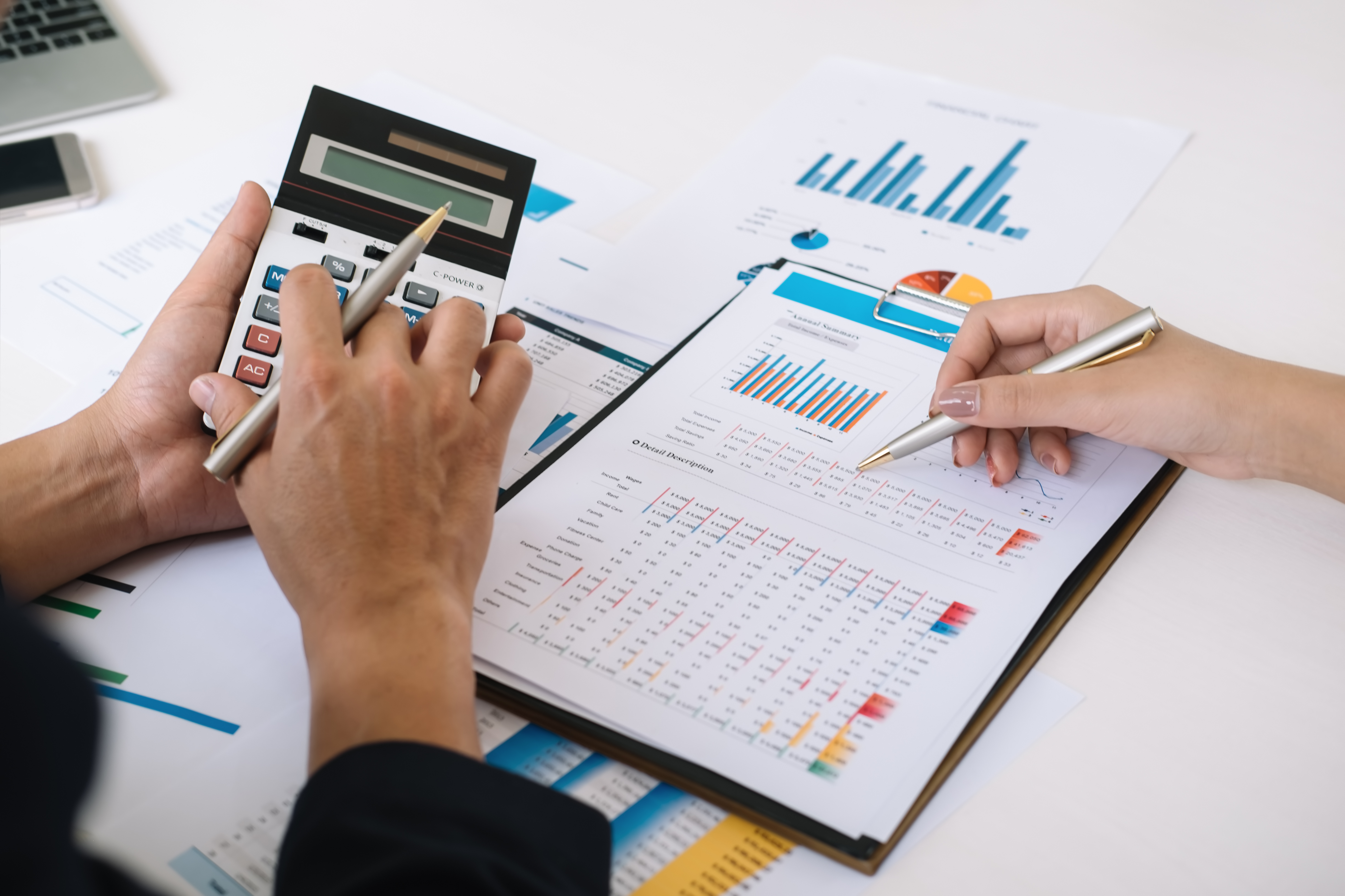 Spreadsheets and graphs with one person holding a calculator, and another person writing