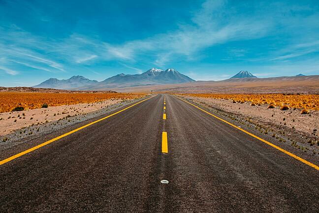 Road stretching out in to the distance with mountains on the horizon on a bright, sunny day.