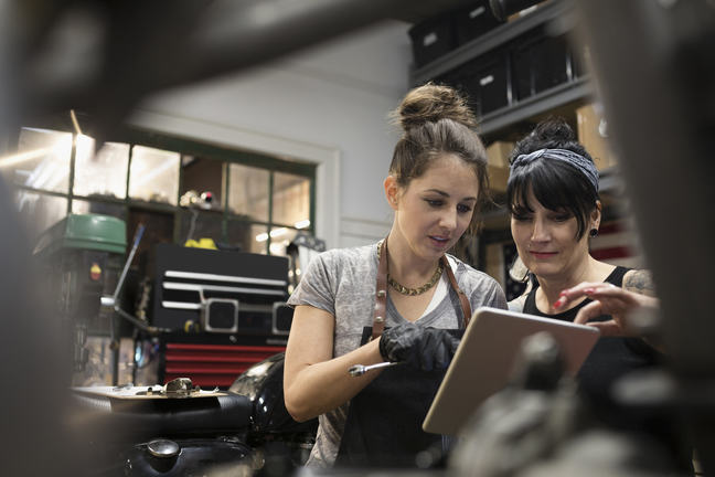 Two women working in a mechanics looking at an iPad to assist them with their work.