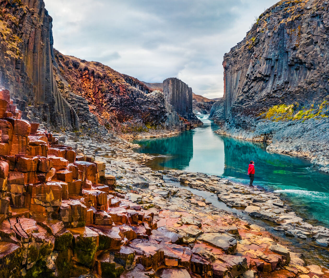 Person at the bottom of a canyon surrounded by basalt columns. View from flying drone of Studlagil Canyon.