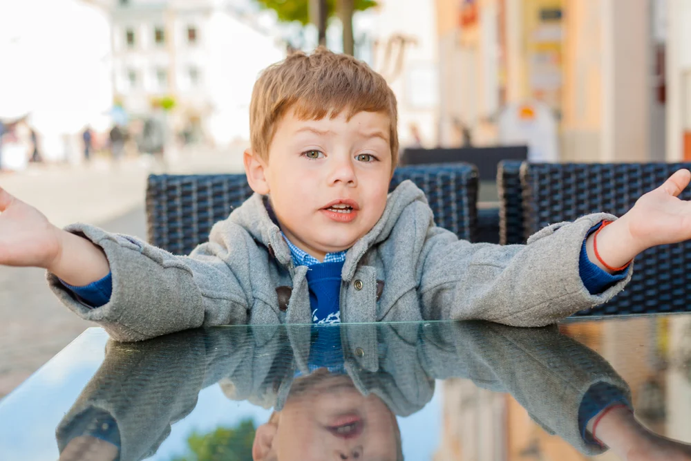 Young boy sitting at cafe table with arms open