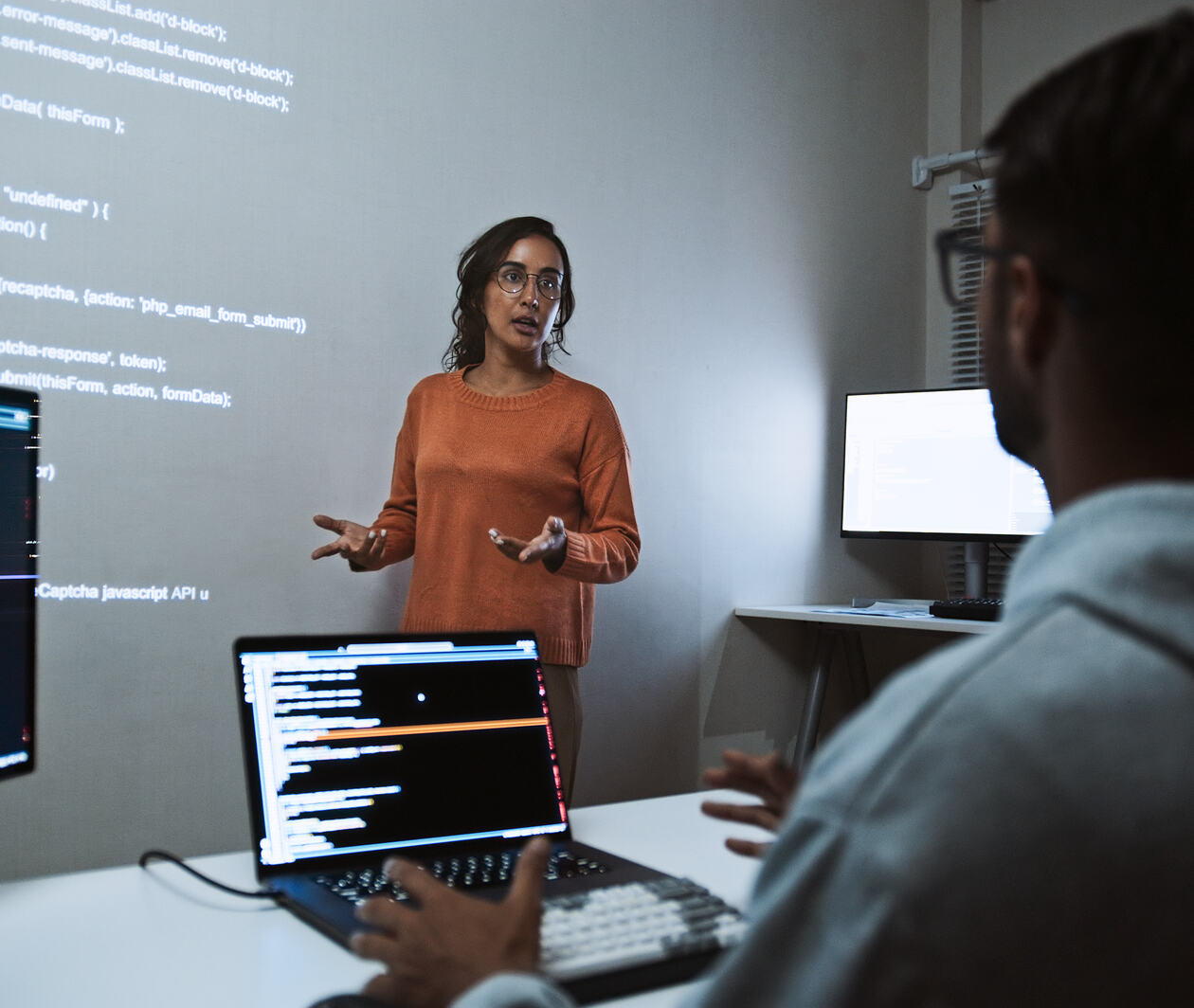 Woman teaching at the front of a seminar room, while the student takes notes on two monitors