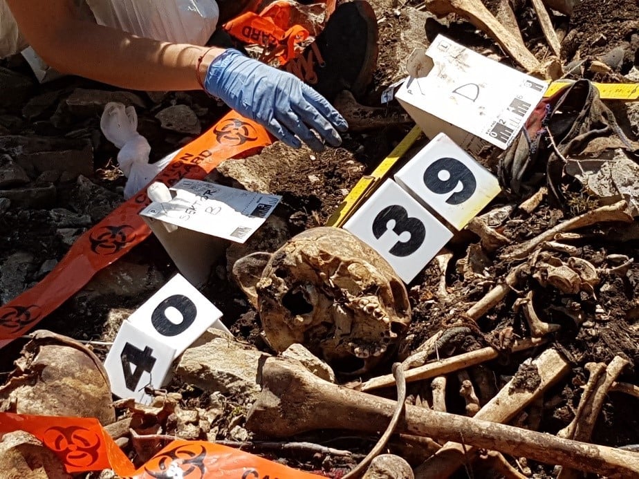 A pile of disarticulated human remains at the base of a cliff. Some numbers and some tape have been placed nearby to record the remains