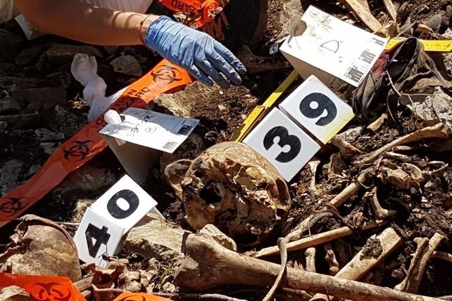 A pile of disarticulated human remains at the base of a cliff. Some numbers and some tape have been placed nearby to record the remains