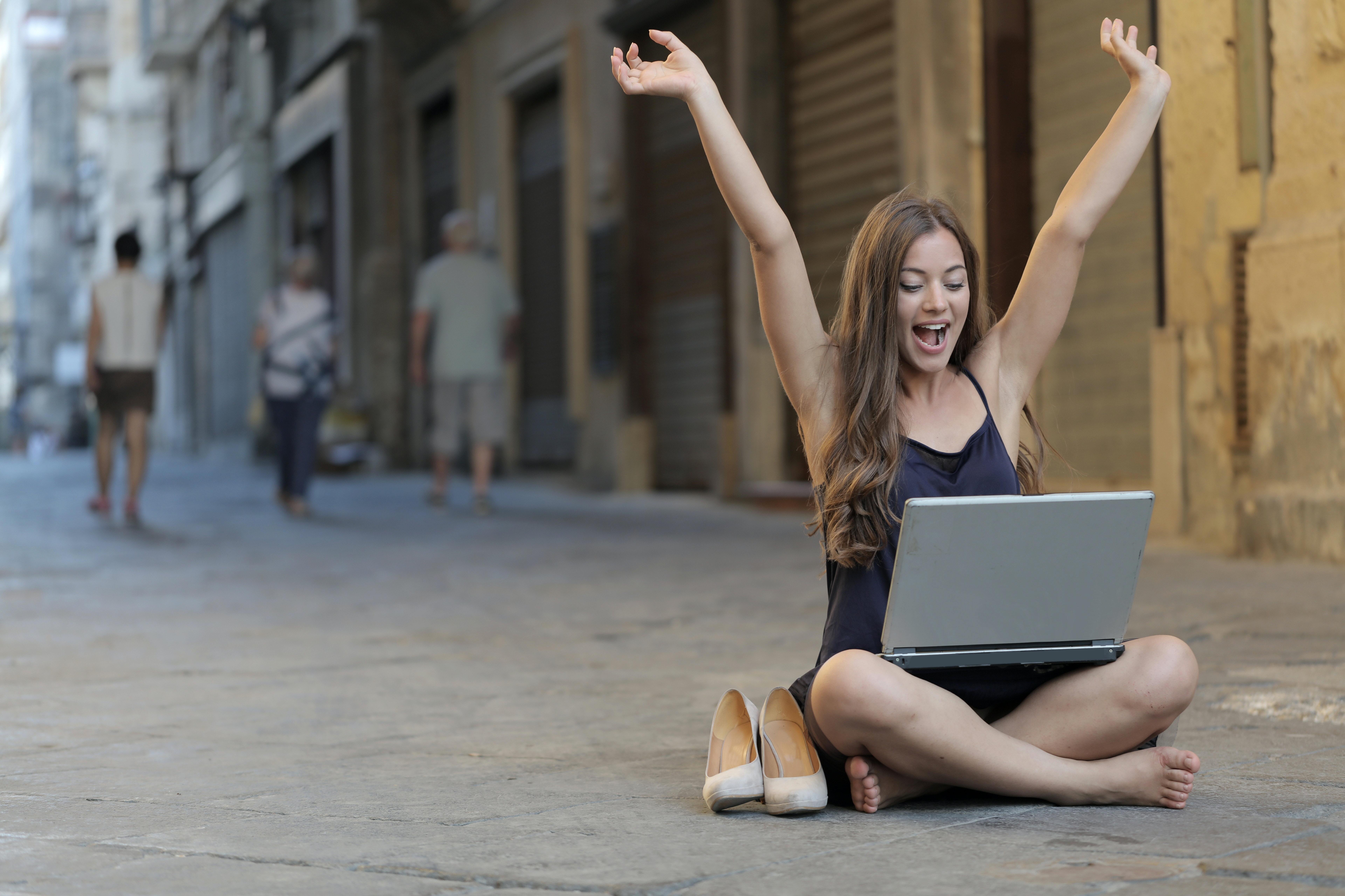 A girl sitting on the street with laptop feeling happy