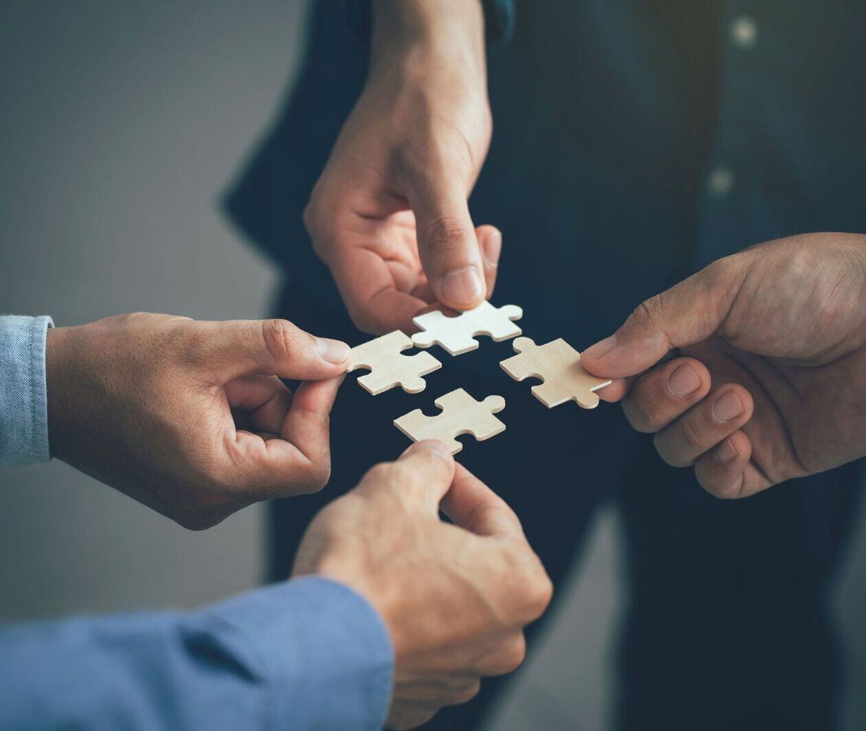 Four hands holding puzzle pieces that fit together.