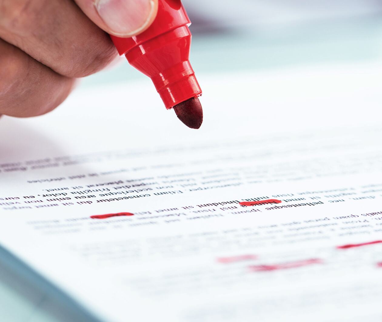 A hand writing with a red marker pen on a piece of paper. 