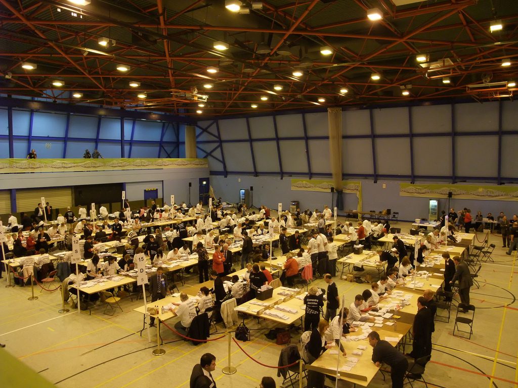 Overhead view of auditorium on election night with votes been sorted and counted by volunteers at tables