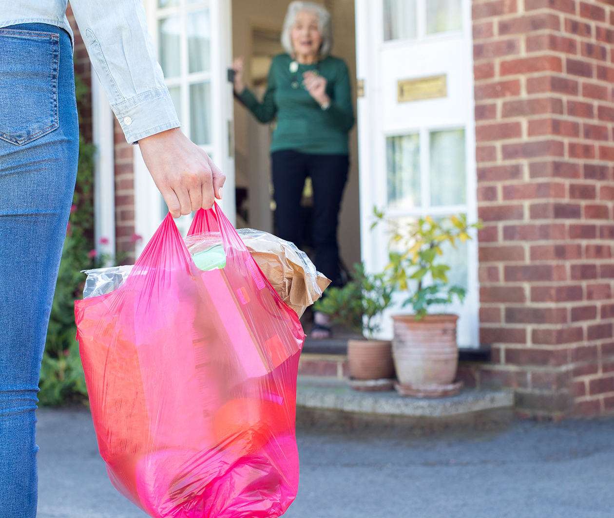 A woman arrives with a full bag of shopping at another woman's door