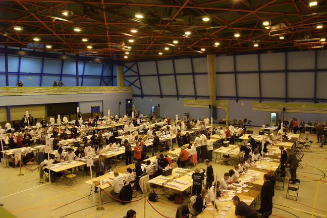Overhead view of auditorium on election night with votes been sorted and counted by volunteers at tables