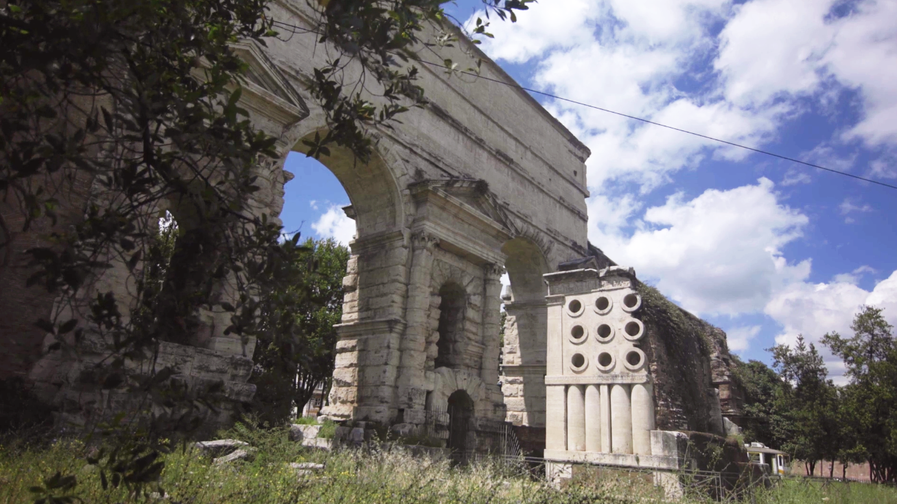 A photo of a square tomb that is next to a large arch.