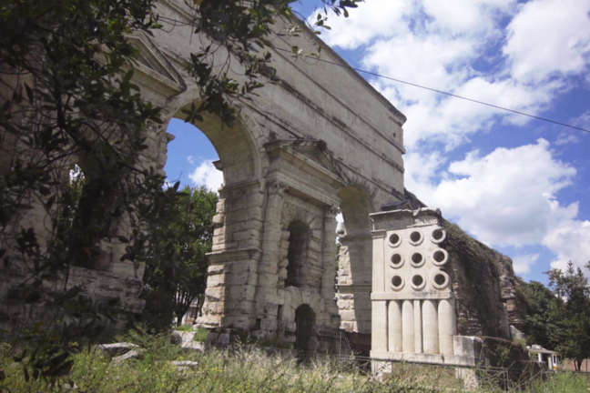 A photo of a square tomb that is next to a large arch.