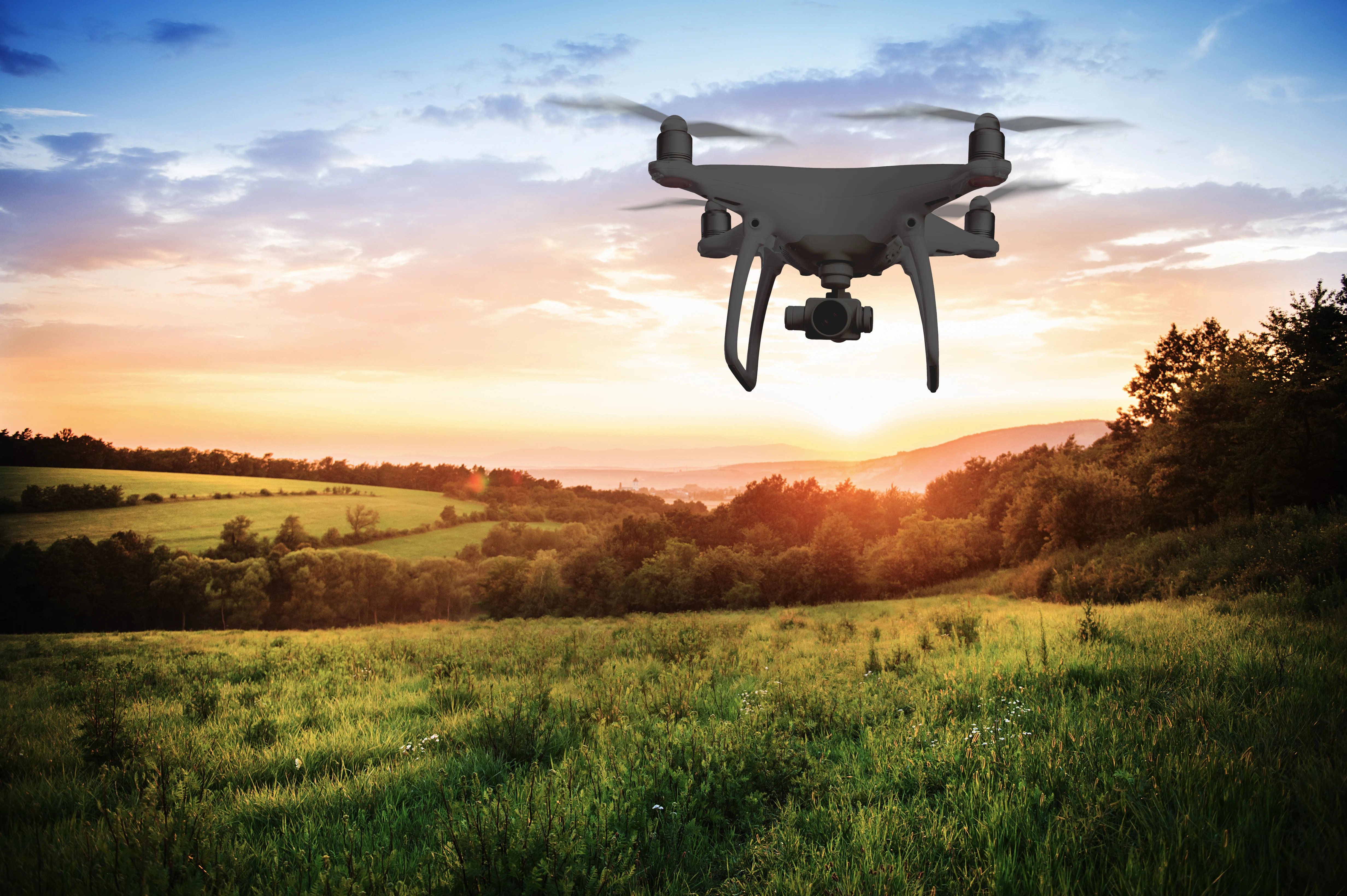 Silhouette of hovering drone taking pictures of green meadows and hills at sunset