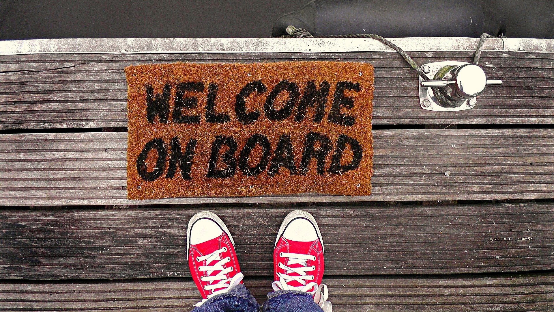 A doormat which says 'Welcome on Board'. Twp feet standing beside it.