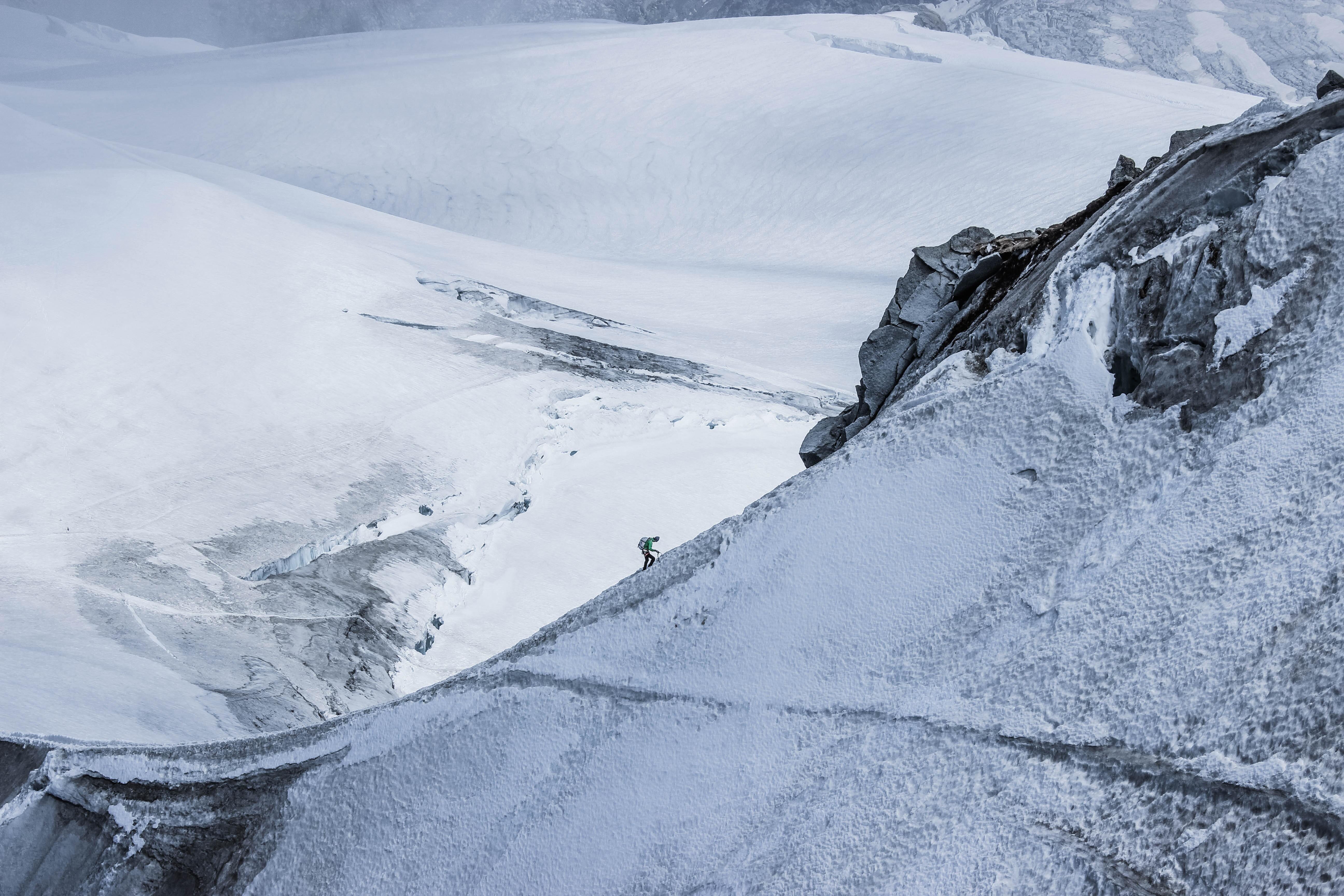 A person climbing a big mountain covered by snow.