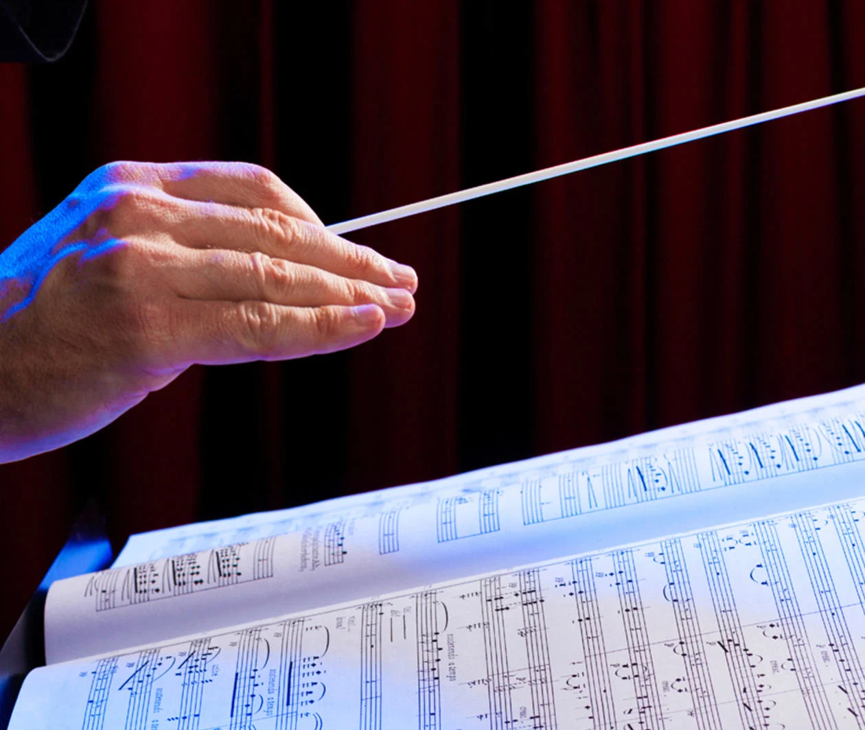 A photograph of a conductor’s hand over the notation of a musical score