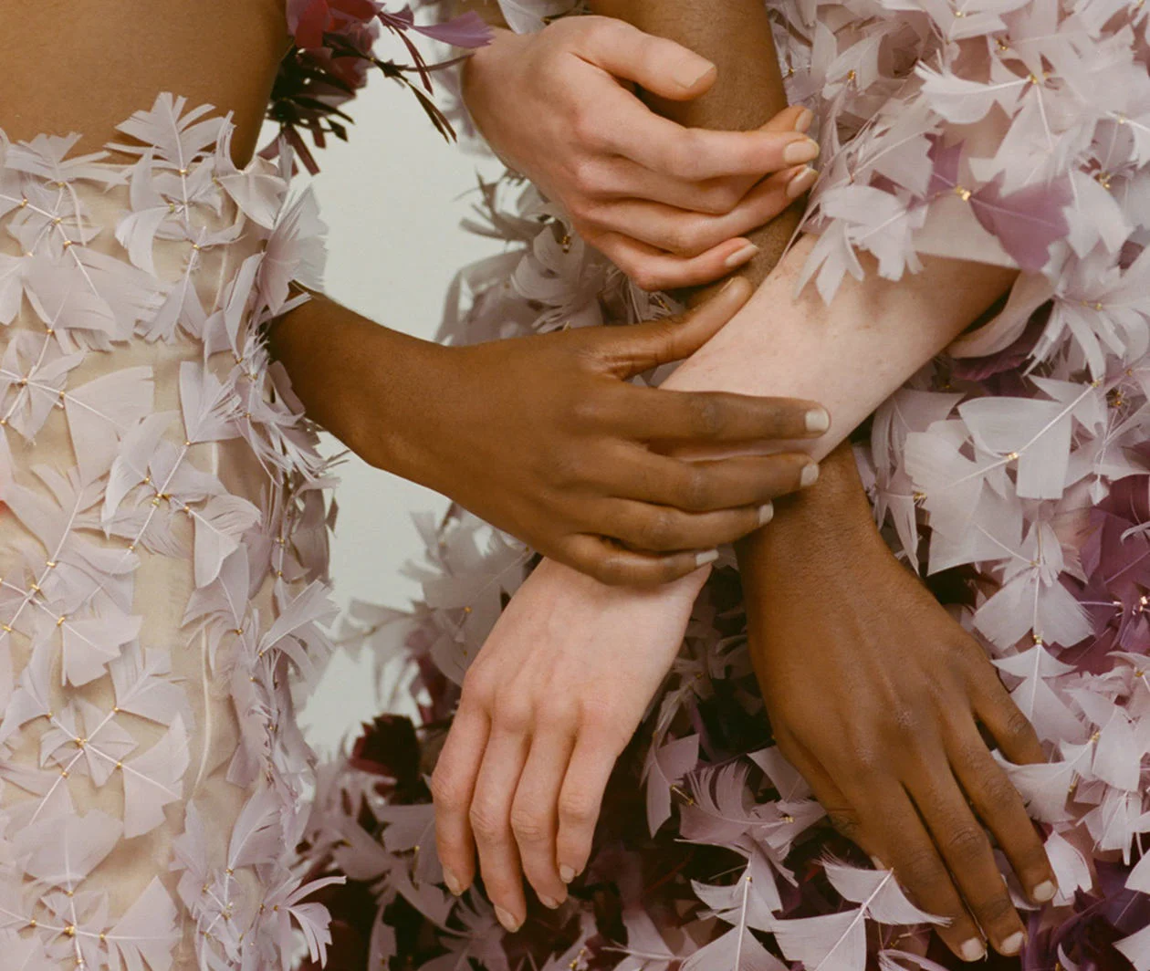 A diverse group of hands holding each other over a feathered gown. The photograph is from the University of the Arts, London, 2018.