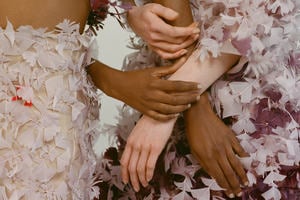 A diverse group of hands holding each other over a feathered gown. The photograph is from the University of the Arts, London, 2018.