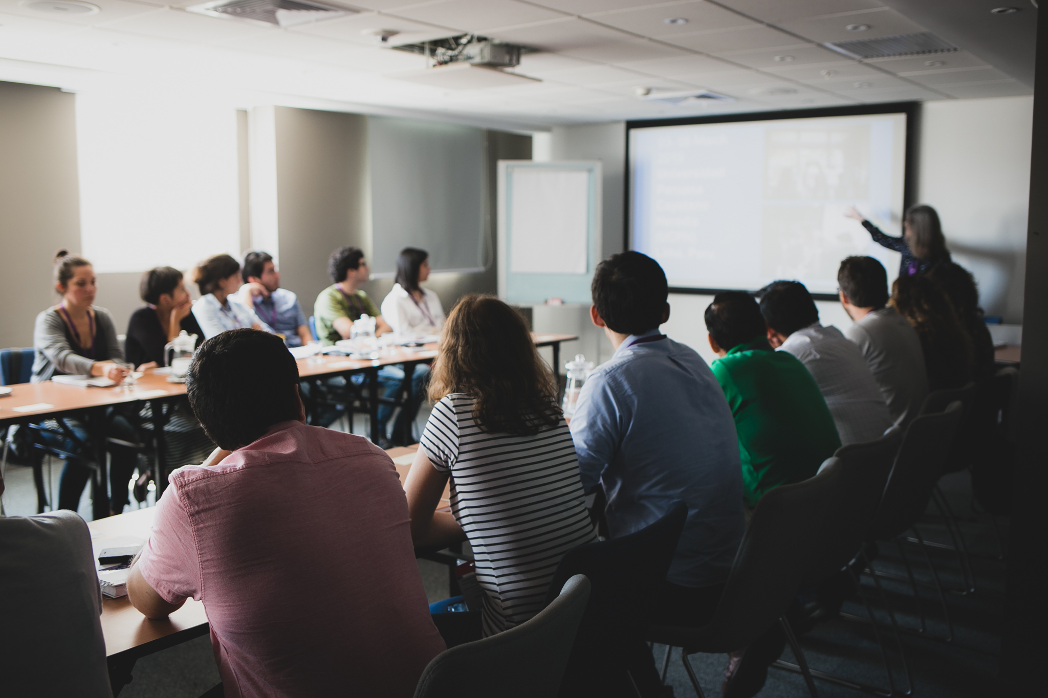 group of learners sitting around U shaped tables listening to the teacher standing at the board