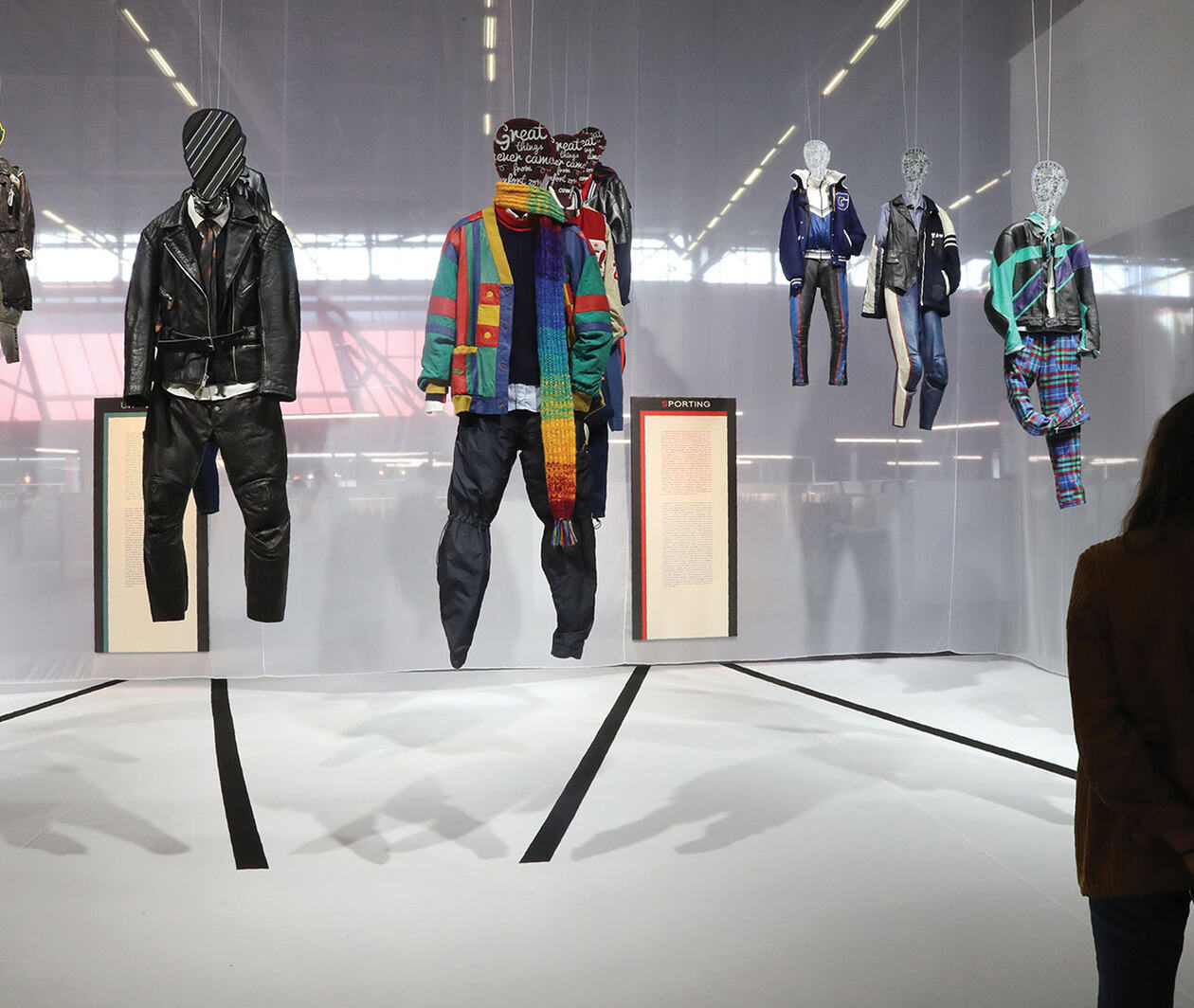 Mannequins with clothes of different styles and textiles hang on display in a gallery.