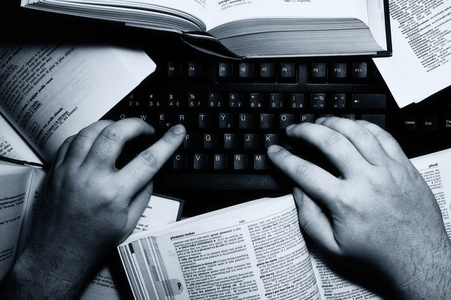 A person typing on a computer surrounded by books.