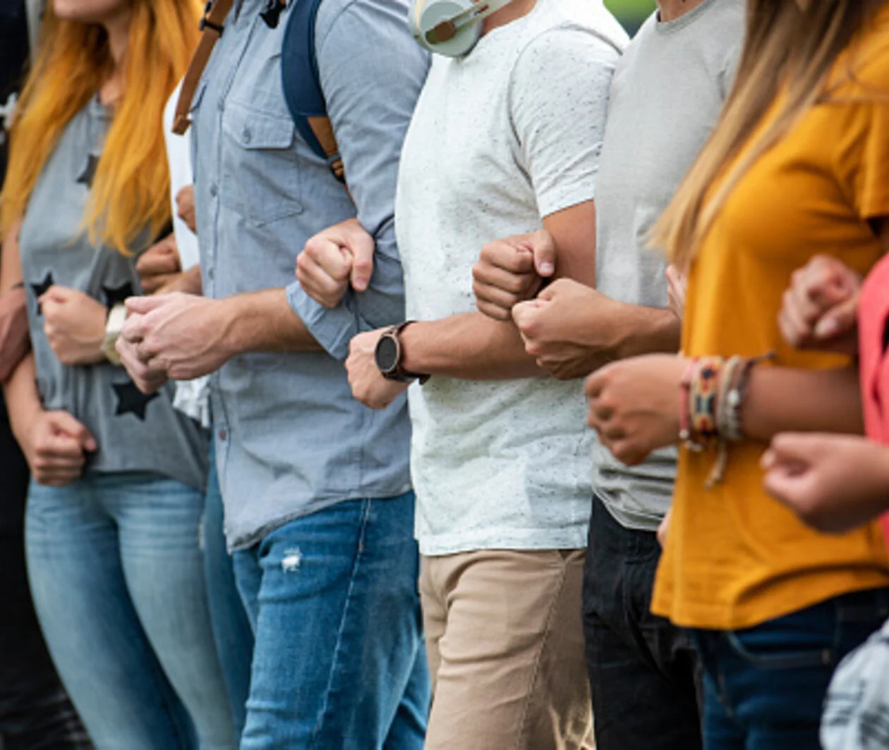 Group of young male and female protestors with arms in arms and clenching fist while standing together outdoors