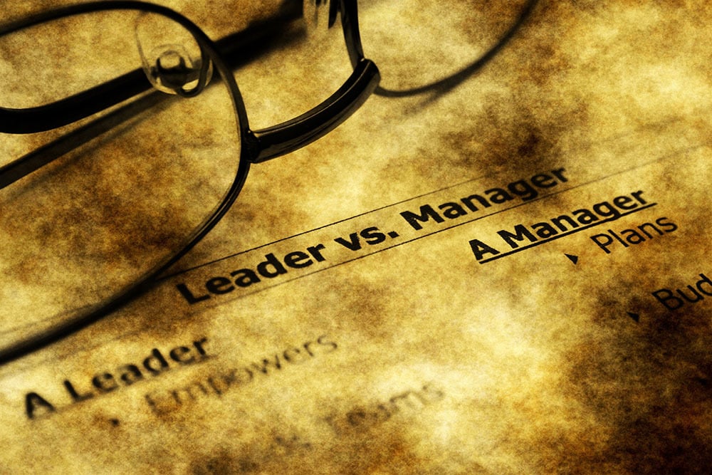 Reading glasses on top of a paper and written on it the words Leader vs Manager