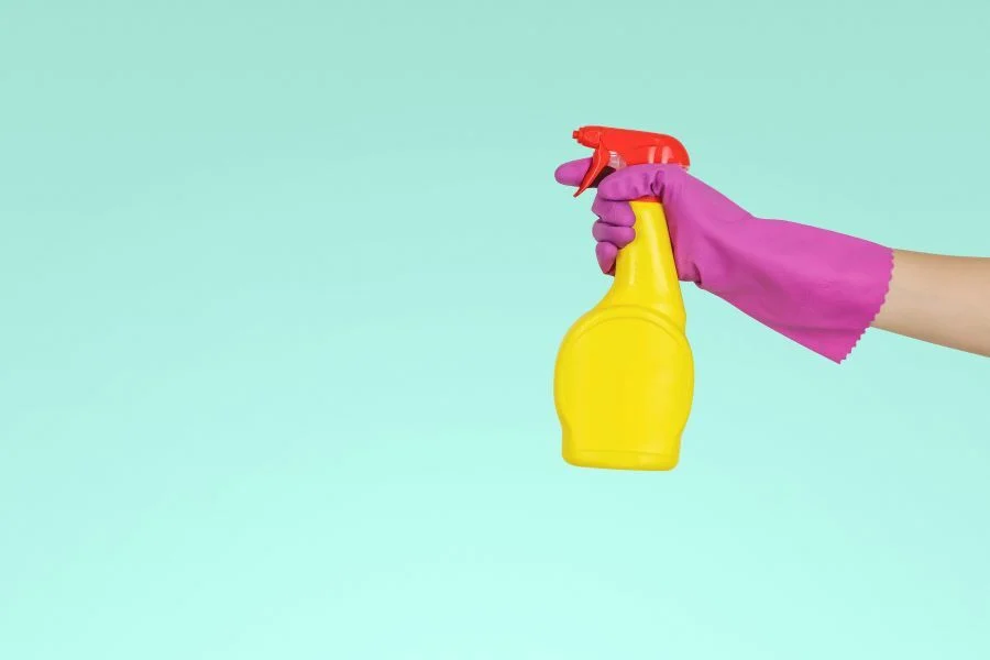 A rubbergloved hand holding a yellow and orange spray bottle