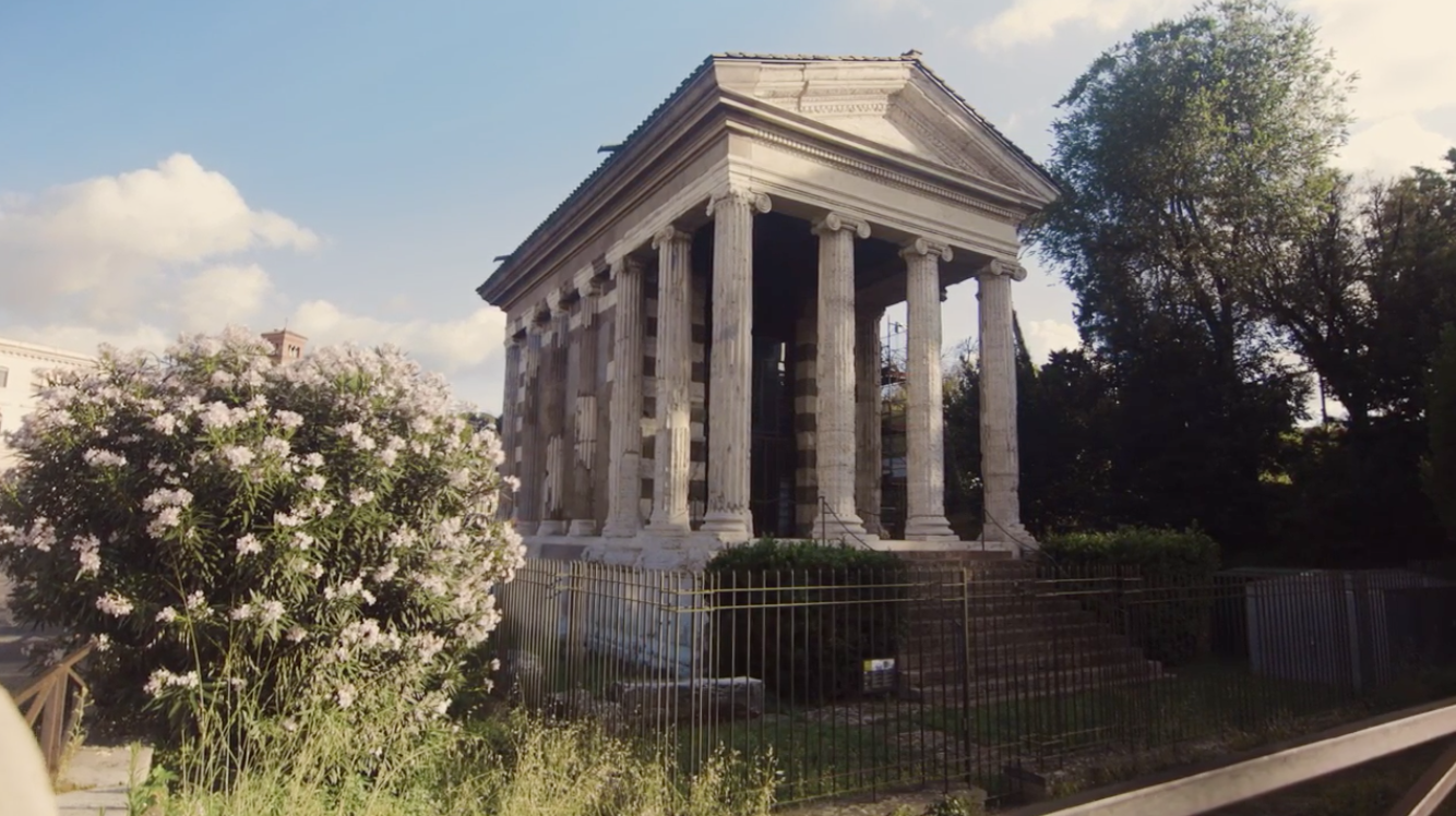 A square temple that's raised from ground level, surrounded by trees and bushes.