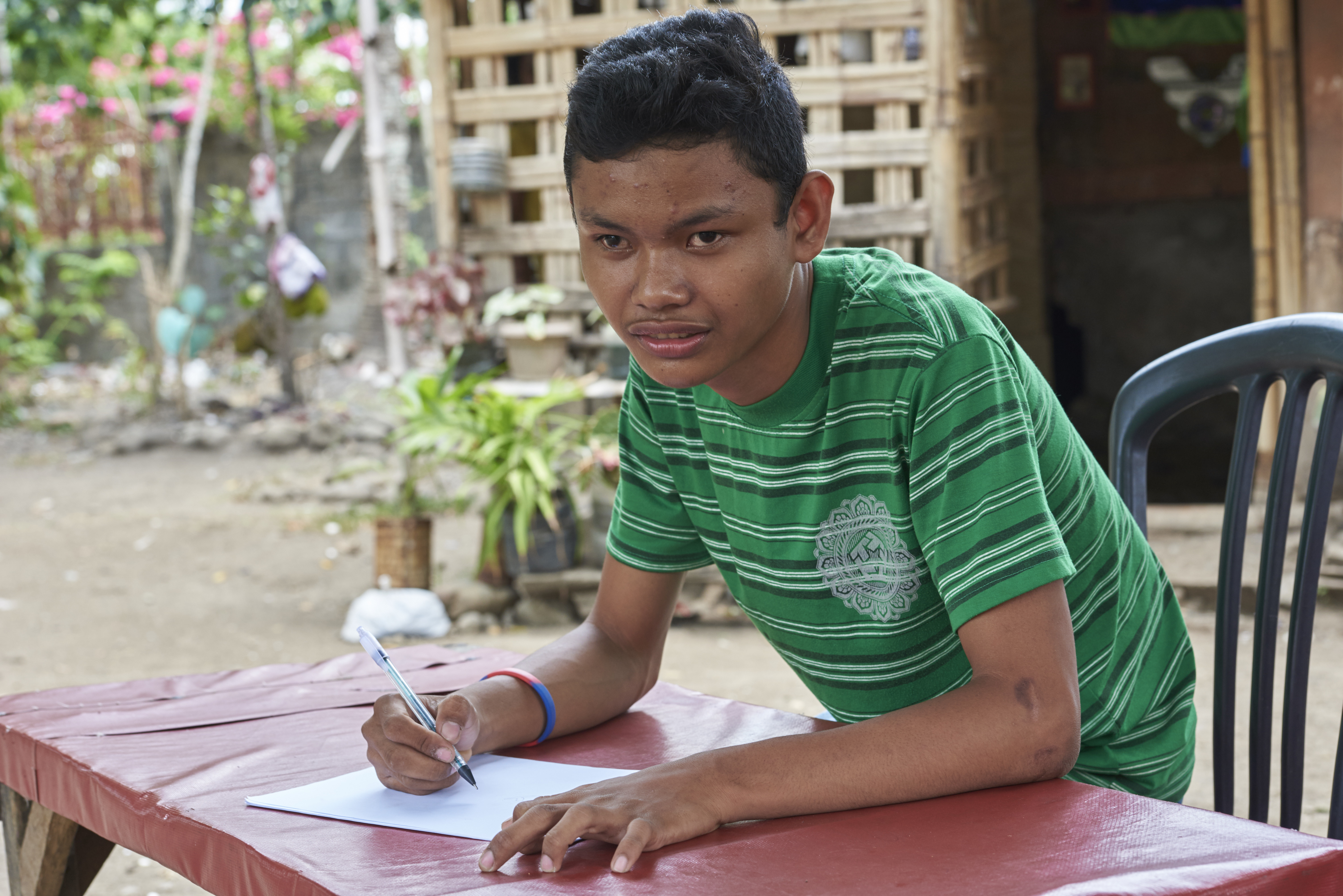 A teenager with cerebral palsy is writing at a table.