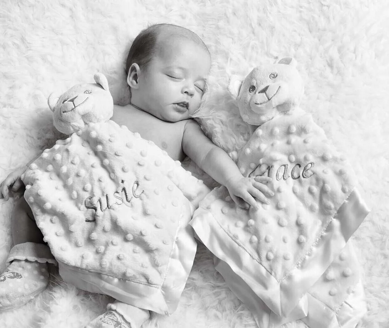 A black and white image of a twin baby laying under a blanket that reads 'Susie' next to a blanket reading 'Grace'. 