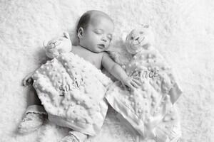 A black and white image of a twin baby laying under a blanket that reads 'Susie' next to a blanket reading 'Grace'. 