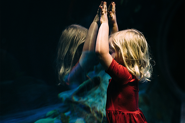 A young girl looking at a reflection of herself