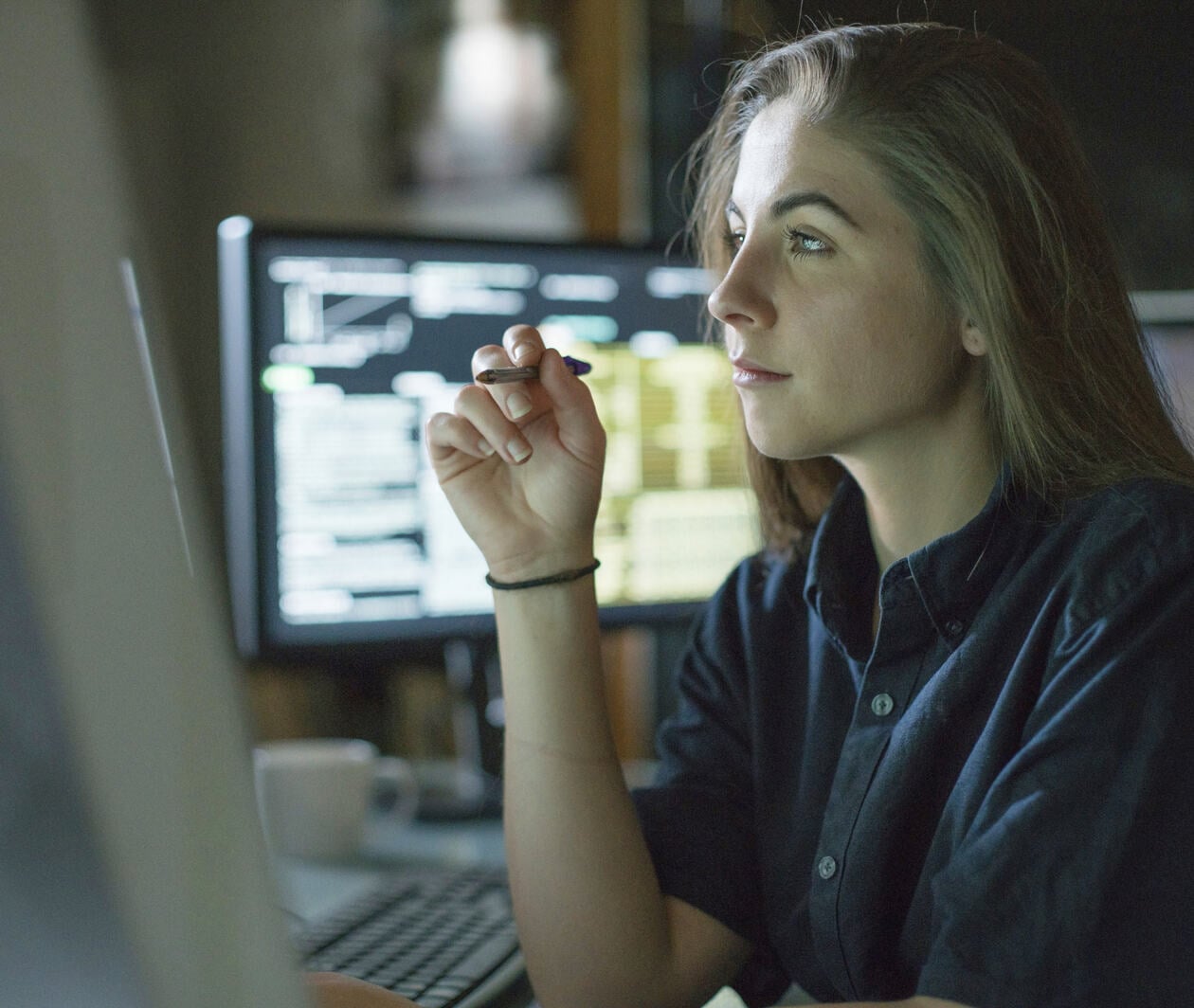 A young woman is seated at a desk surrounded by monitors displaying data.