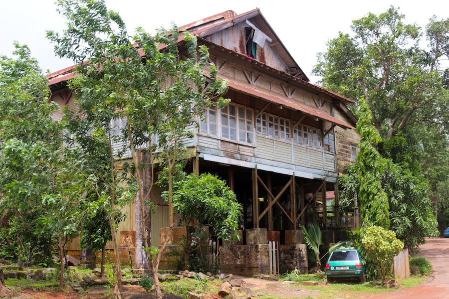 A board house with a car and some trees in the foreground.