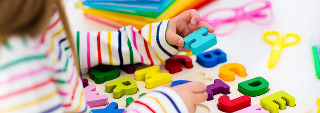 Young girl picking up a blue letter H from a coloured alphabet puzzle.