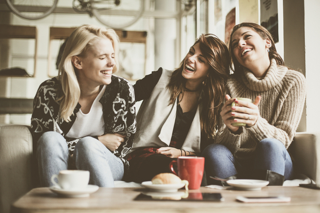 Three laughing and smiling girls sitting on a sofa with coffee