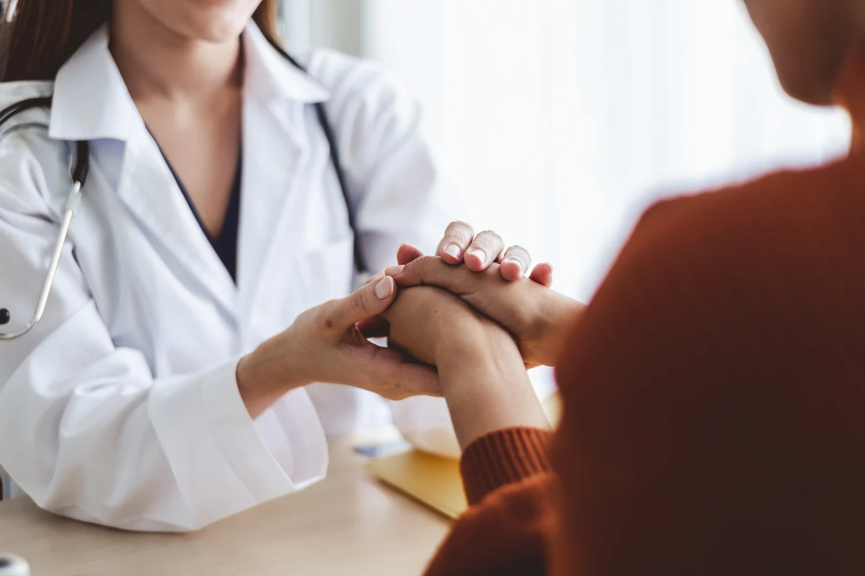 Woman doctor encourages young woman patient by holding hand