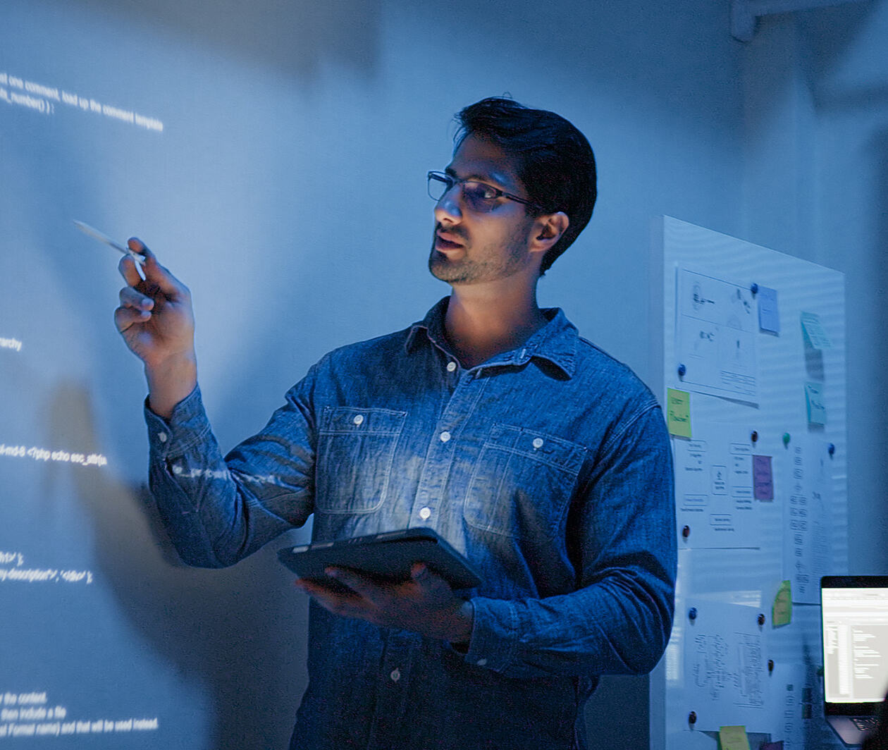 Hispanic Latin American man, software engineer developer use computer projection screen presentation, work on program coding with coworker at night. Programming language development technology concept