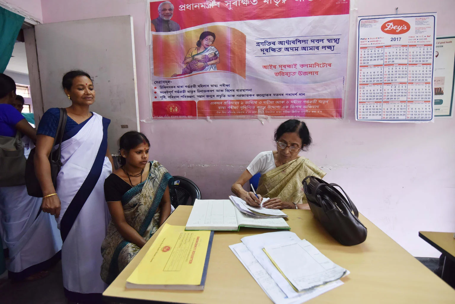 Three women in a room with one, a doctor, writing on a notepad.