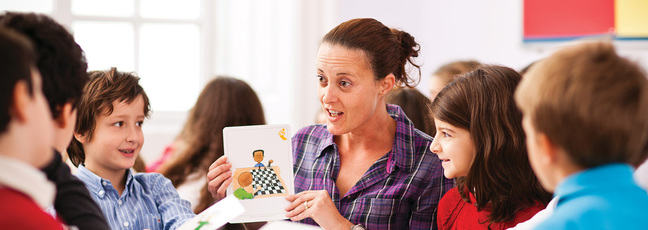 An English language teacher shows a colourful card to a group of young children around her 