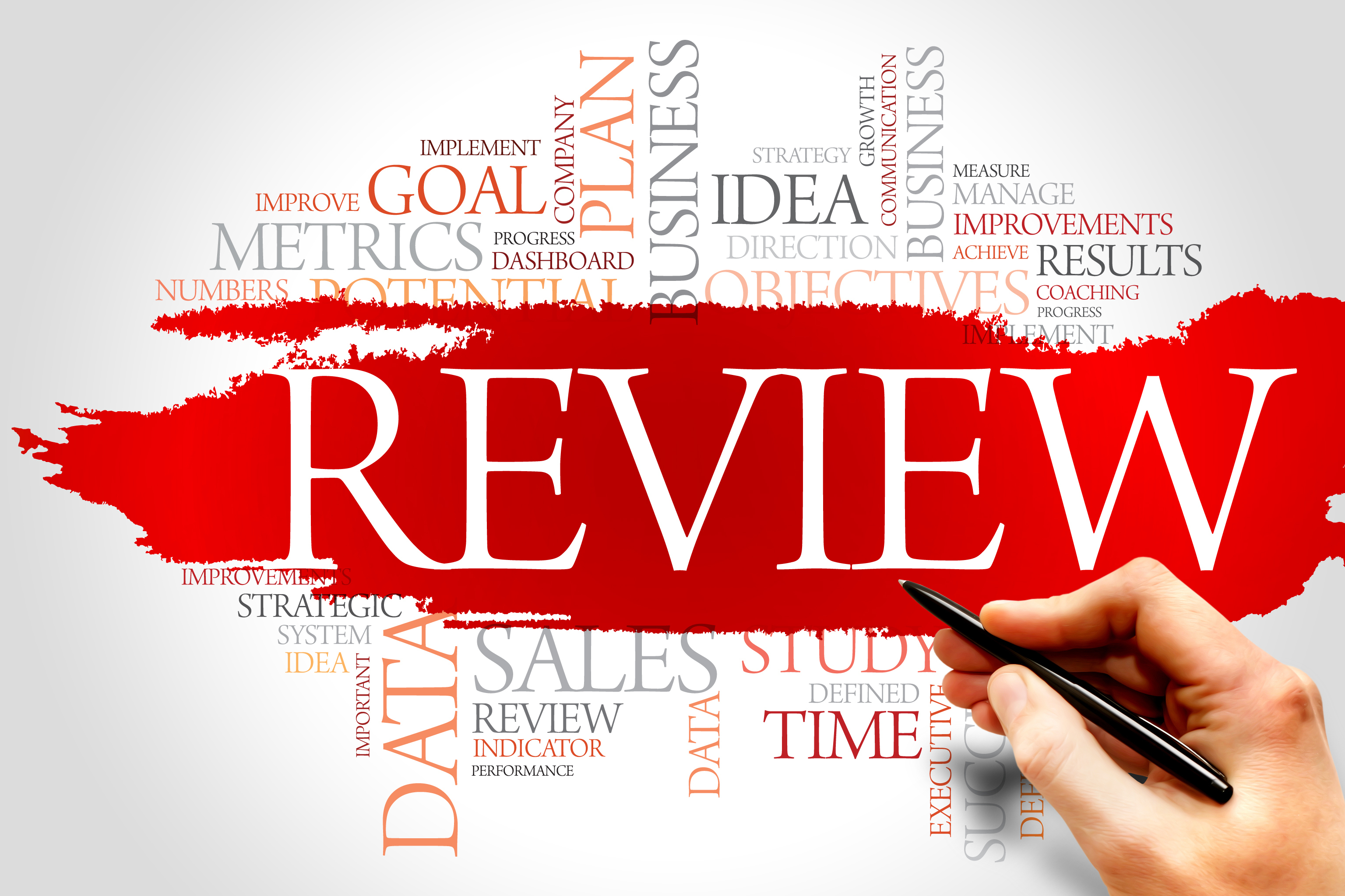 The word Review in big white letters written on a bright red background by a hand holding a pen. Other theme-related words are scattered around it written in duller colours on a white background in a word-web format.