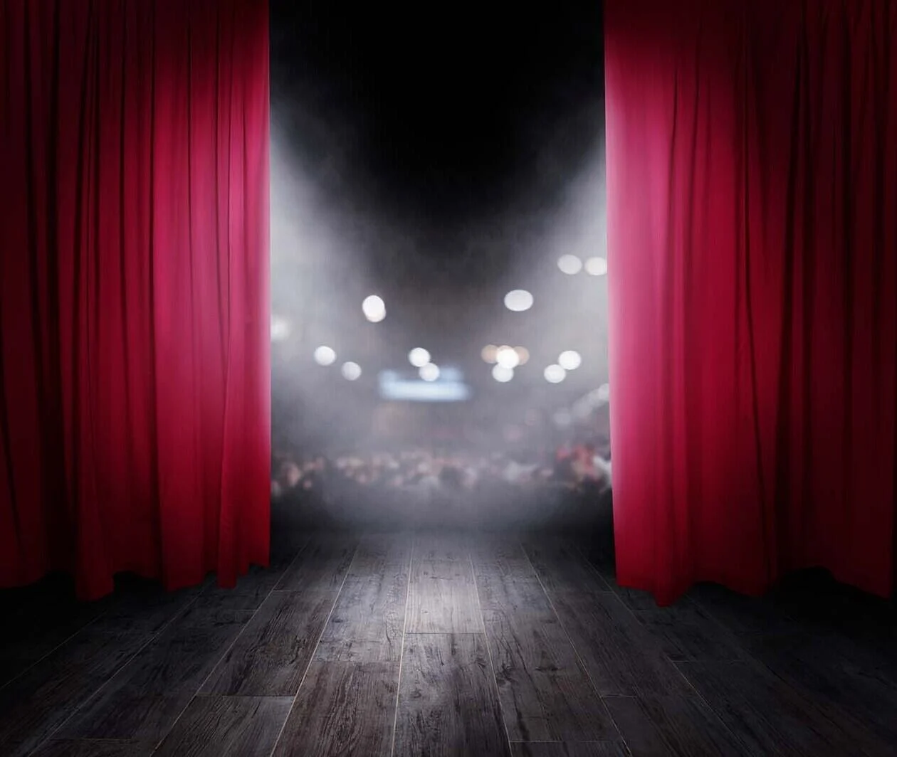 A wooden stage floor with tall dark red draping curtains either side looking out into a dark audience of blurry people and spotlights.