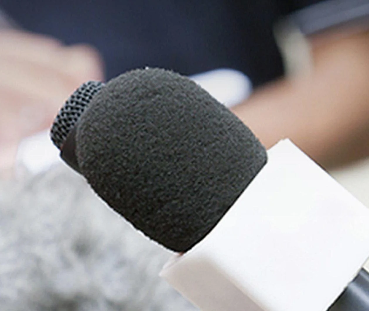 A man being interviewed with microphones in the foreground and people taking notes in the background.