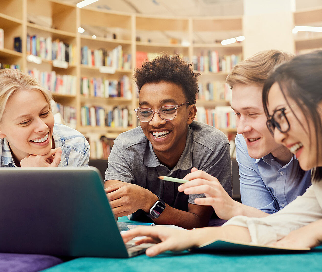 smiling students sat around a laptop in a library