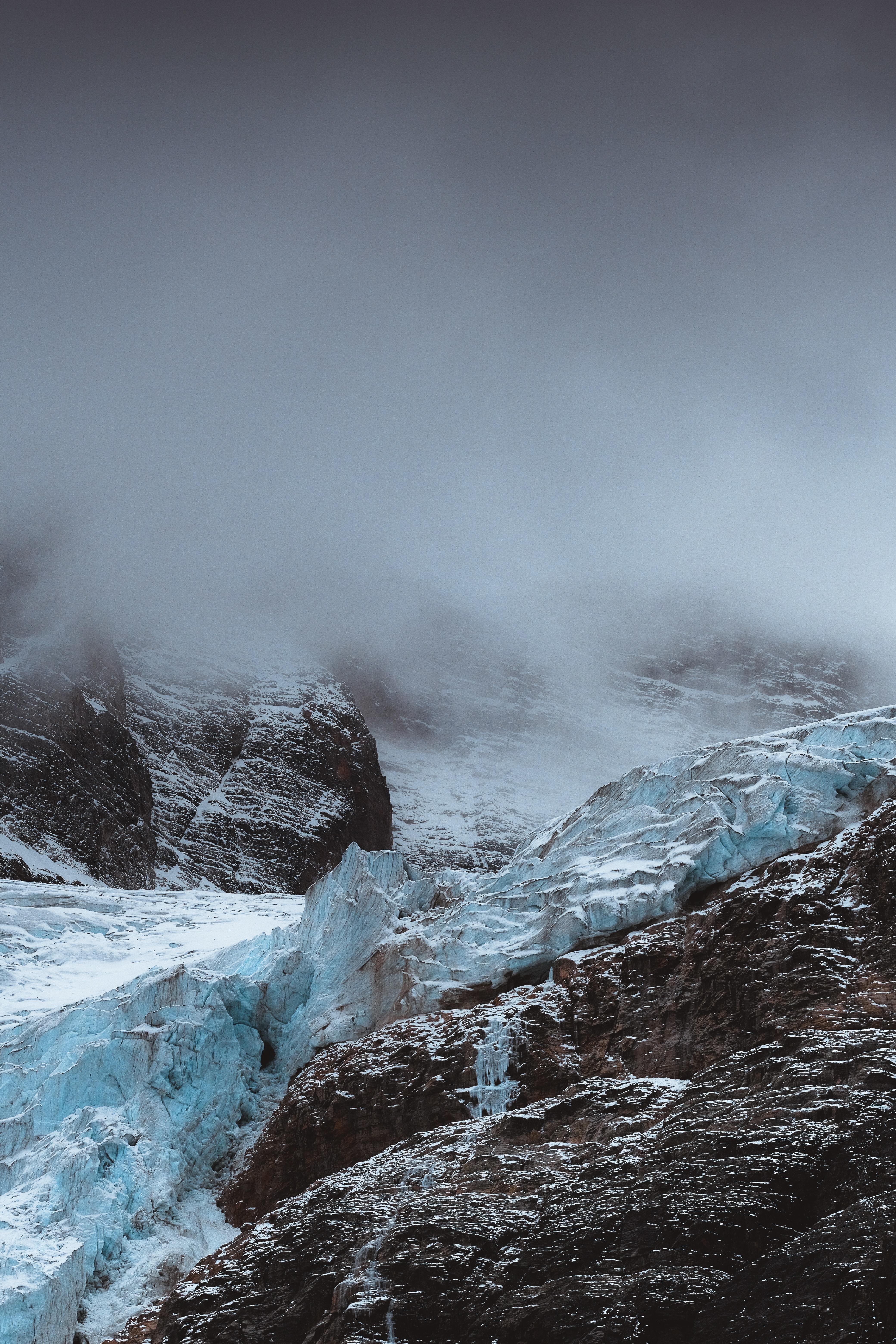 Moody image of mountains shrouded in cloud, with a glacier in the foreground.